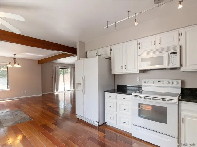 a kitchen with granite countertop a refrigerator stove and white cabinets with wooden floor