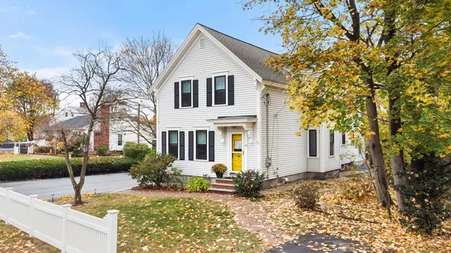 a view of a white house next to a yard with large trees