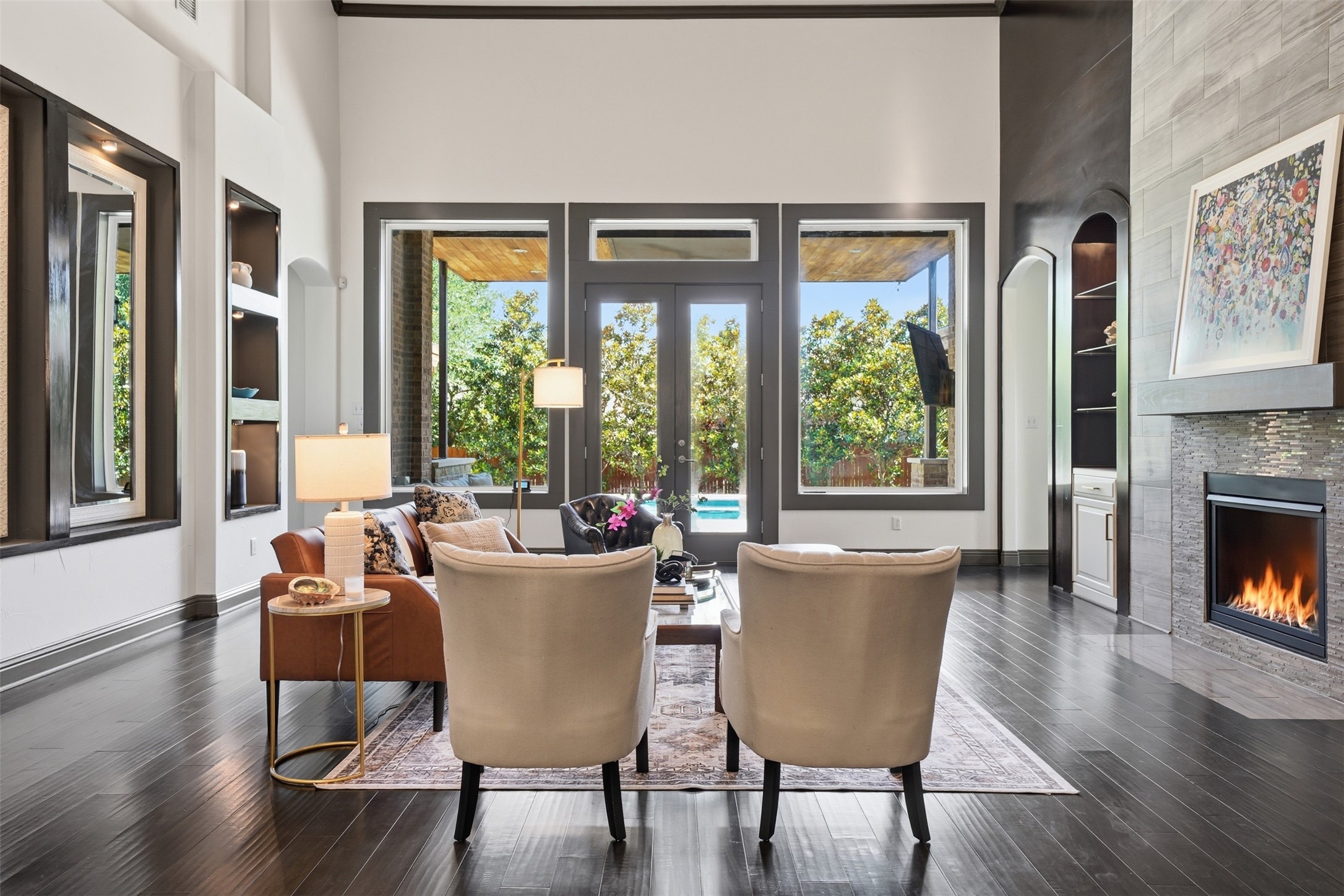 8729 Vantage Point Drive Austin, TX 78737 - Photo 11 of 33 A spacious living room with dark hardwood floors opens to a lush outdoor area with a pool, centered by a contemporary fireplace.