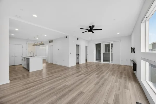 a view of an empty room with wooden floor and a kitchen