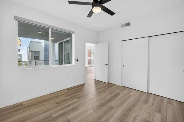 a view of an empty room with wooden floor and a ceiling fan
