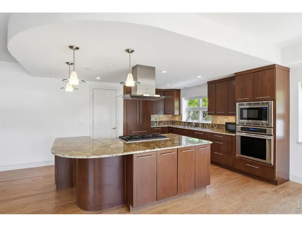 a kitchen with stainless steel appliances kitchen island granite countertop a sink a stove and a wooden cabinets