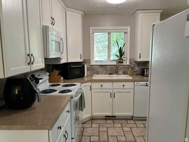7659 State Street Midvale, UT 84047 - Photo 5 of 33 Kitchen with white cabinetry, white appliances, a textured ceiling, tasteful backsplash, and light countertops