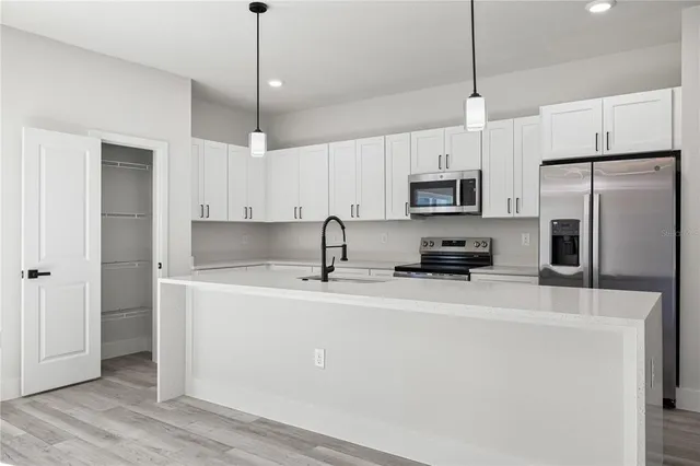 a kitchen with stainless steel appliances a refrigerator a sink a stove a microwave and island with wooden floor