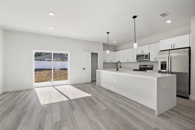 a large white kitchen with stainless steel appliances granite countertop a refrigerator a oven a sink and white cabinets with wooden floor