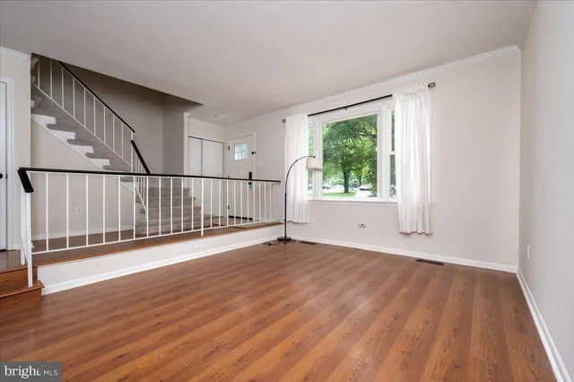 a view of an empty room with wooden floor and fan
