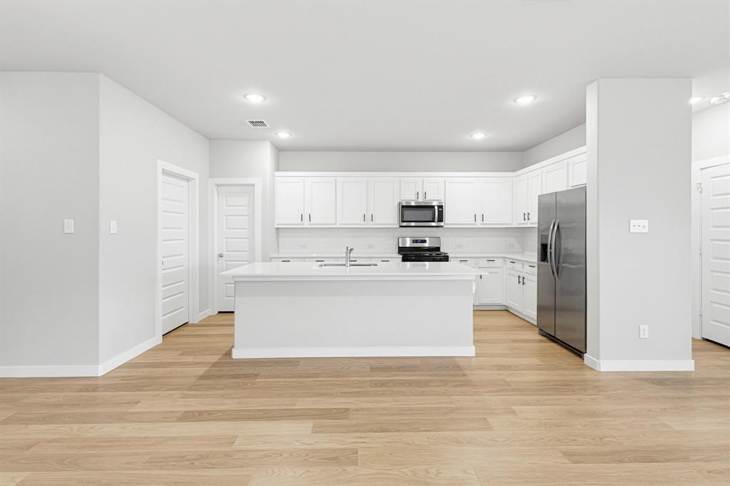 2108 Mossfield Lane Forney, TX 75126 - Photo 3 of 28 Open-concept kitchen featuring an island with a sink, white cabinetry, stainless steel appliances, recessed lighting, and wood-finish flooring