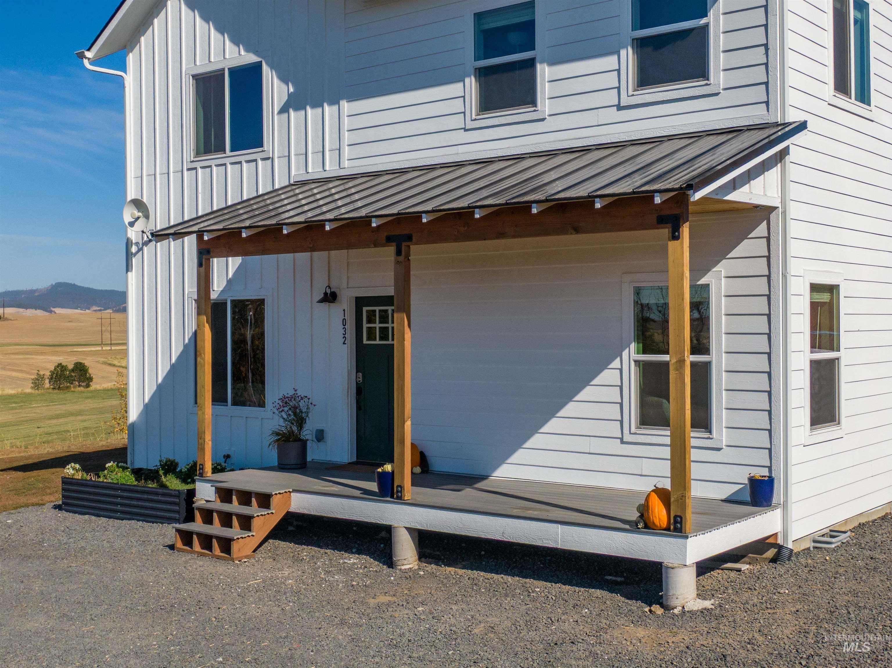 White horizontal siding exterior with board and batten accents, a dark green entry door with windowpanes, a covered porch with a metal roof, and wood support beams