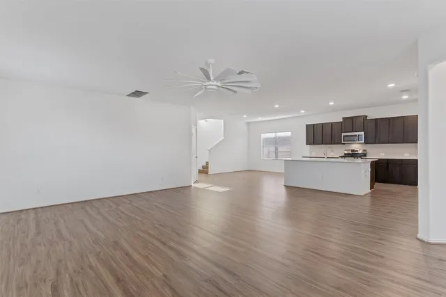 an empty room with wooden floor chandelier fan and windows