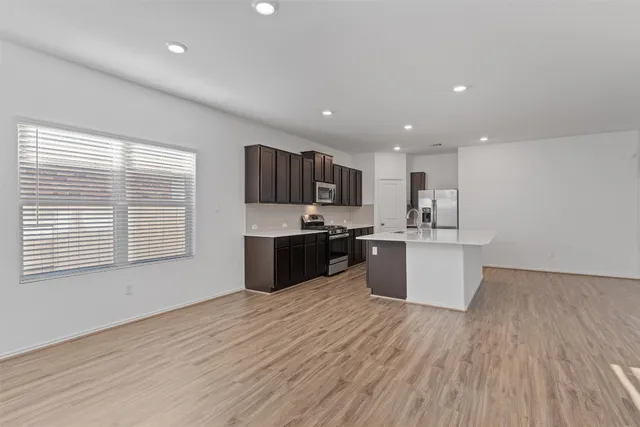 a large kitchen with stainless steel appliances granite countertop a large counter top a wooden floors and a large window