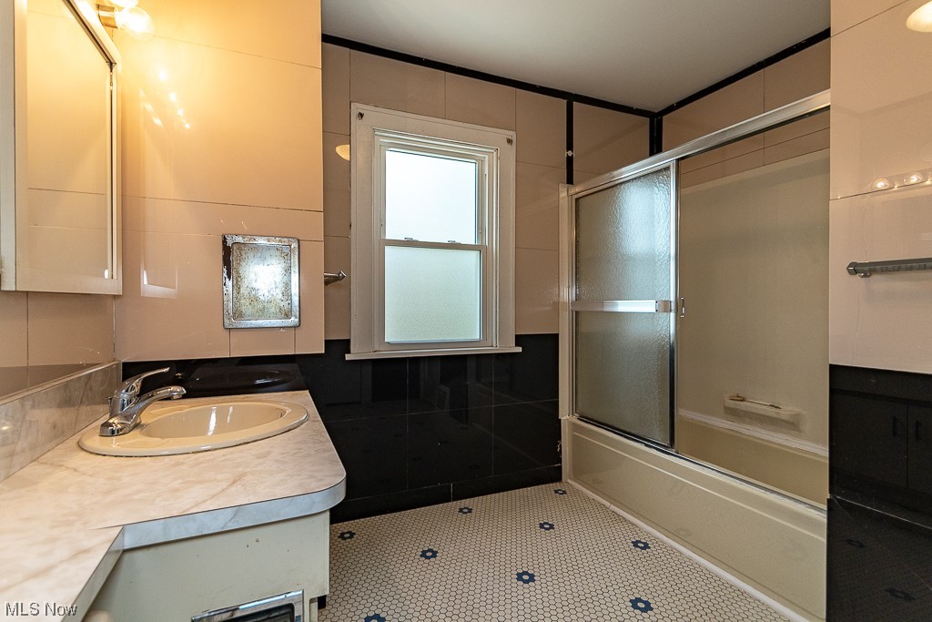 29396 Detroit Road Westlake, OH 44145 - Photo 25 of 30 Bathroom featuring combined tub/ shower with glass door, vanity with extensive cabinet space, tile walls, and tile floors