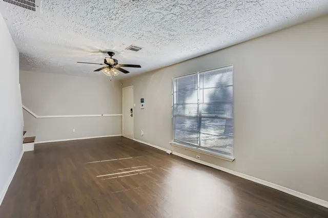 an empty room with wooden floor fan and windows