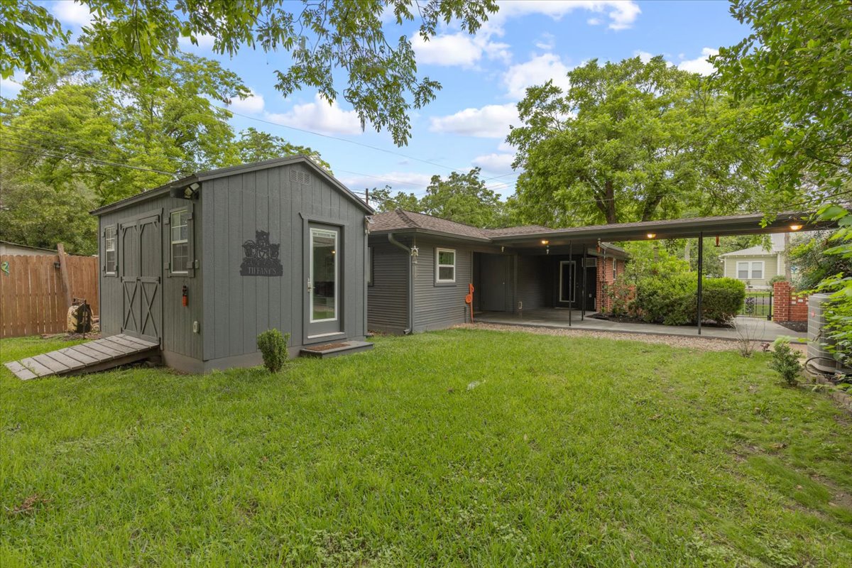 607 Short Street Smithville, TX 78957 - Photo 28 of 31 Expansive grassy yard featuring a detached shed with double barn doors and a glass-paneled entry door, a covered carport, and mature perimeter trees