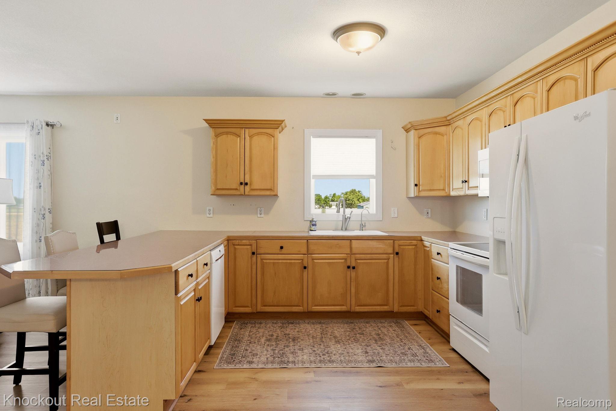9941 Lange Road Birch Run, MI 48415 - Photo 12 of 42 Kitchen featuring light wood cabinetry, white appliances, a peninsula with seating, a window above the sink, and wood-finish flooring