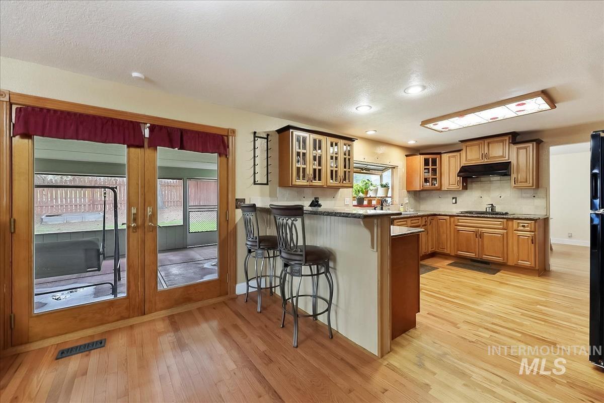 11875 West Hidden Valley Rim Road Boise, ID 83709 - Photo 5 of 36 Kitchen featuring glass insert cabinets, a kitchen bar, light wood finished floors, a peninsula, and recessed lighting