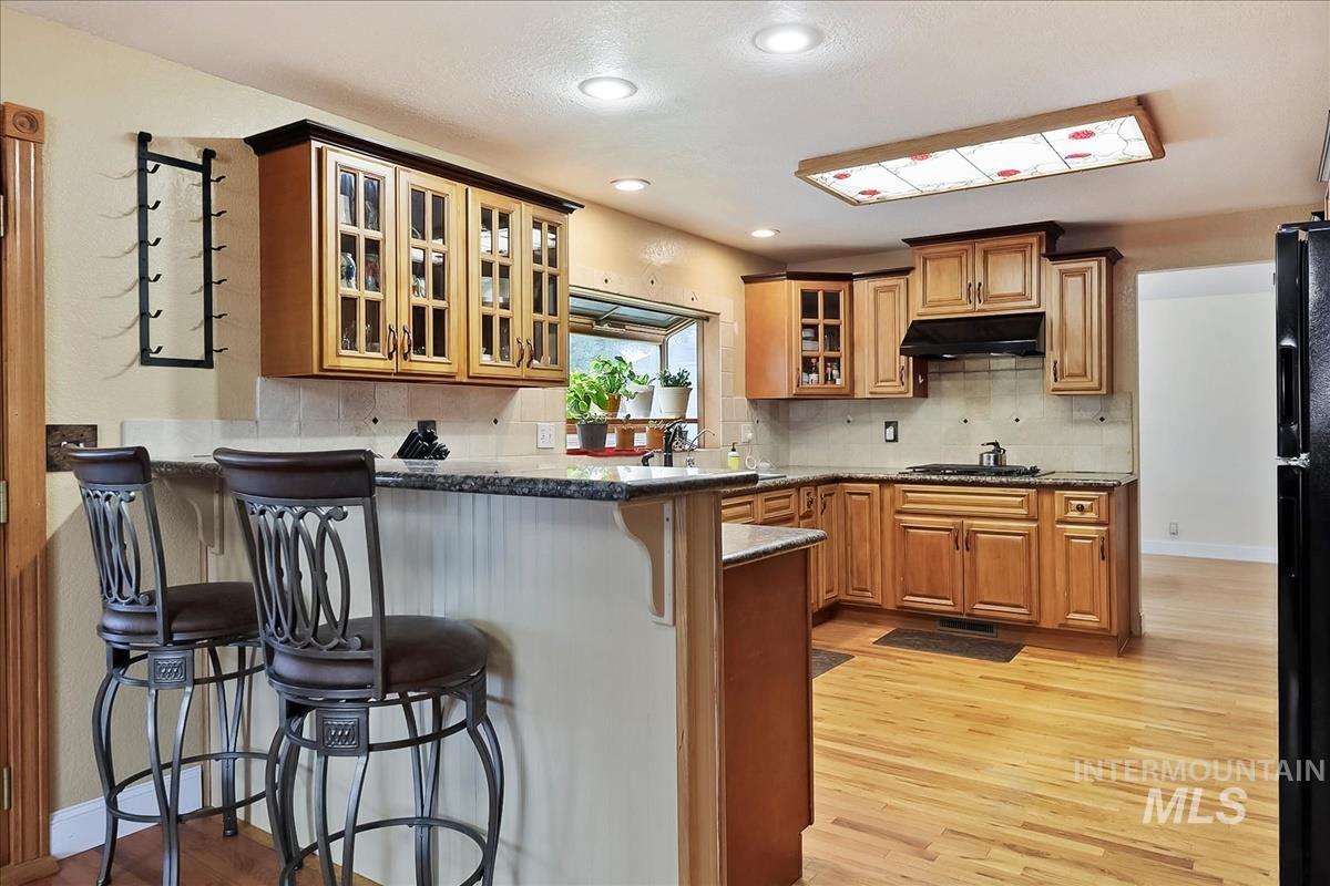 11875 West Hidden Valley Rim Road Boise, ID 83709 - Photo 6 of 36 Kitchen with glass insert cabinets, light wood-style floors, a breakfast bar area, dark stone counters, and recessed lighting