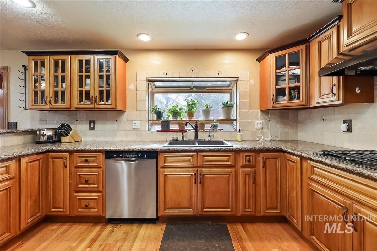 11875 West Hidden Valley Rim Road Boise, ID 83709 - Photo 8 of 36 Kitchen with glass fronted cabinets, stainless steel dishwasher, light stone counters, wood finish cabinets, and recessed lighting