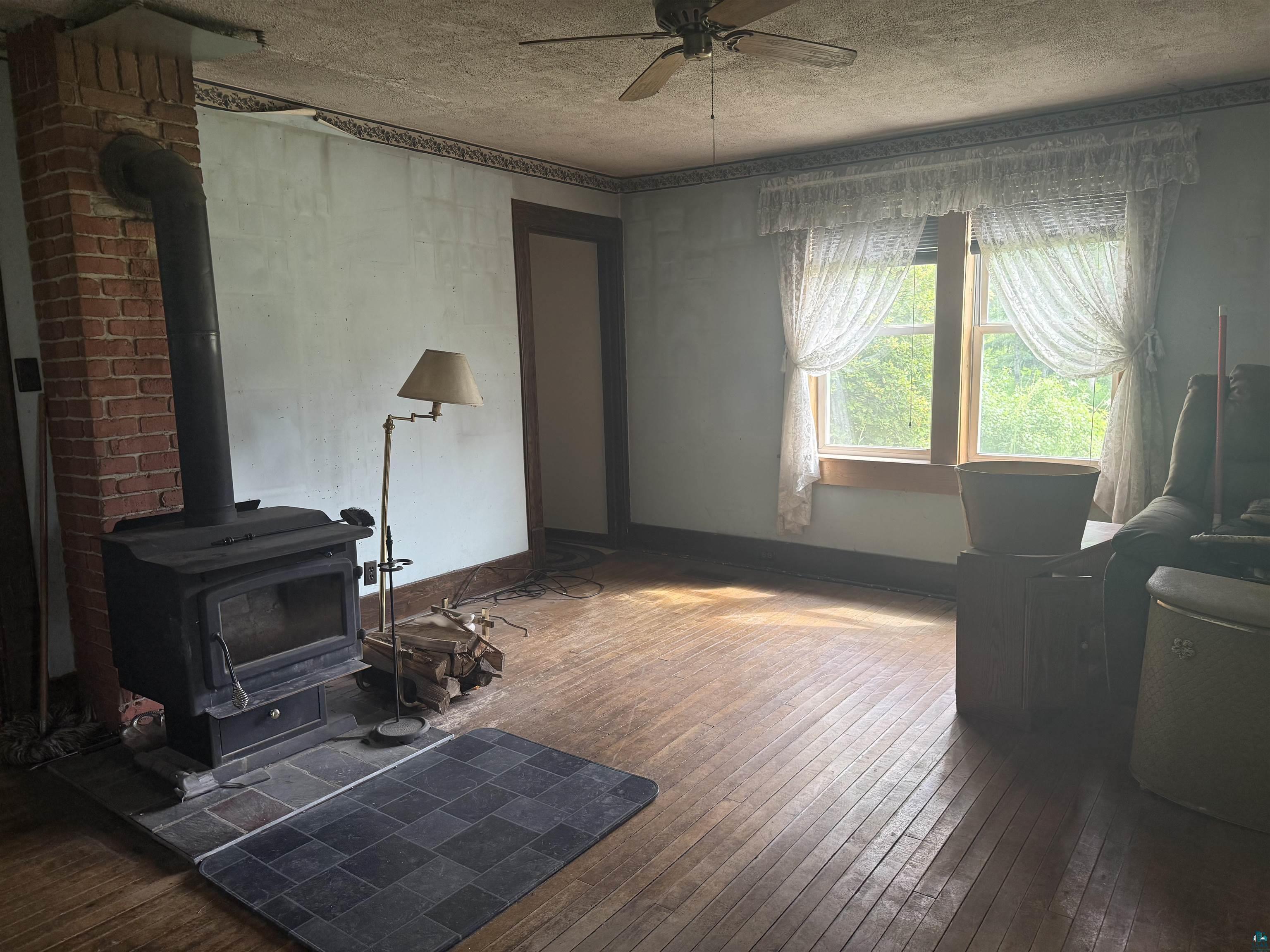3541 Bent Trout Lake Road Barnum, MN 55707 - Photo 14 of 41 Interior space featuring a brick-clad wood-burning stove with a slate tile hearth, wood-finish flooring, a ceiling fan, and double windows with wood trim
