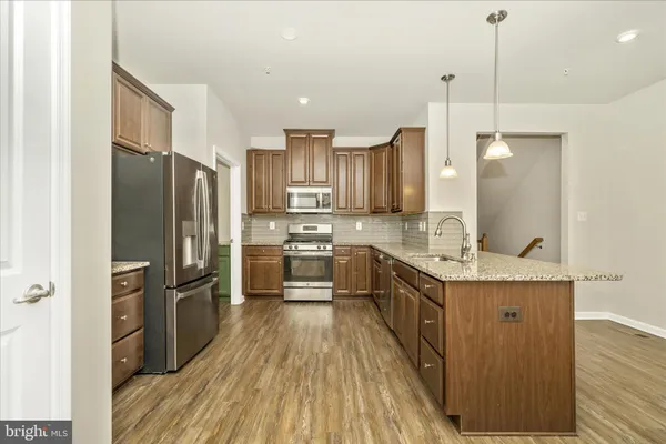 a kitchen with stainless steel appliances granite countertop a refrigerator a sink dishwasher a stove and a wooden floor