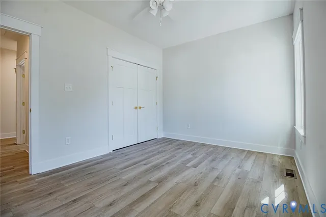 a view of an empty room with wooden floor and a ceiling fan