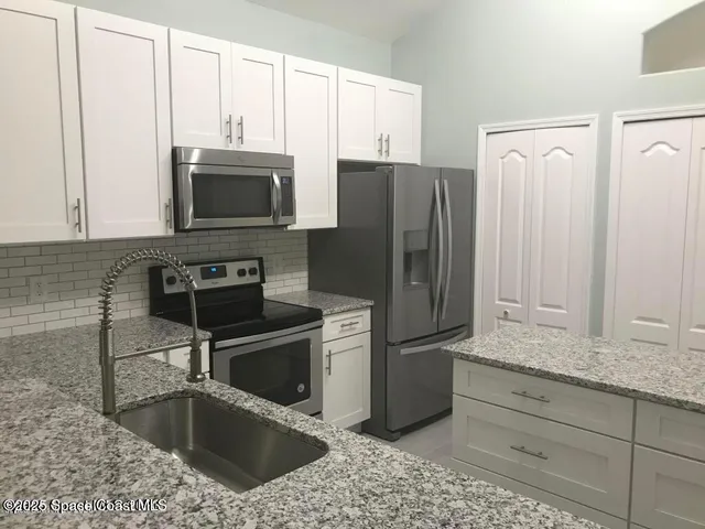 a kitchen with stainless steel appliances granite countertop a refrigerator a stove a sink and white cabinets