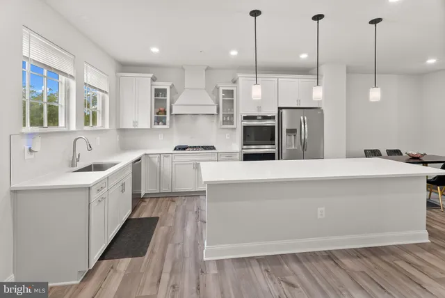 a large kitchen with kitchen island a large counter top a sink stainless steel appliances and cabinets