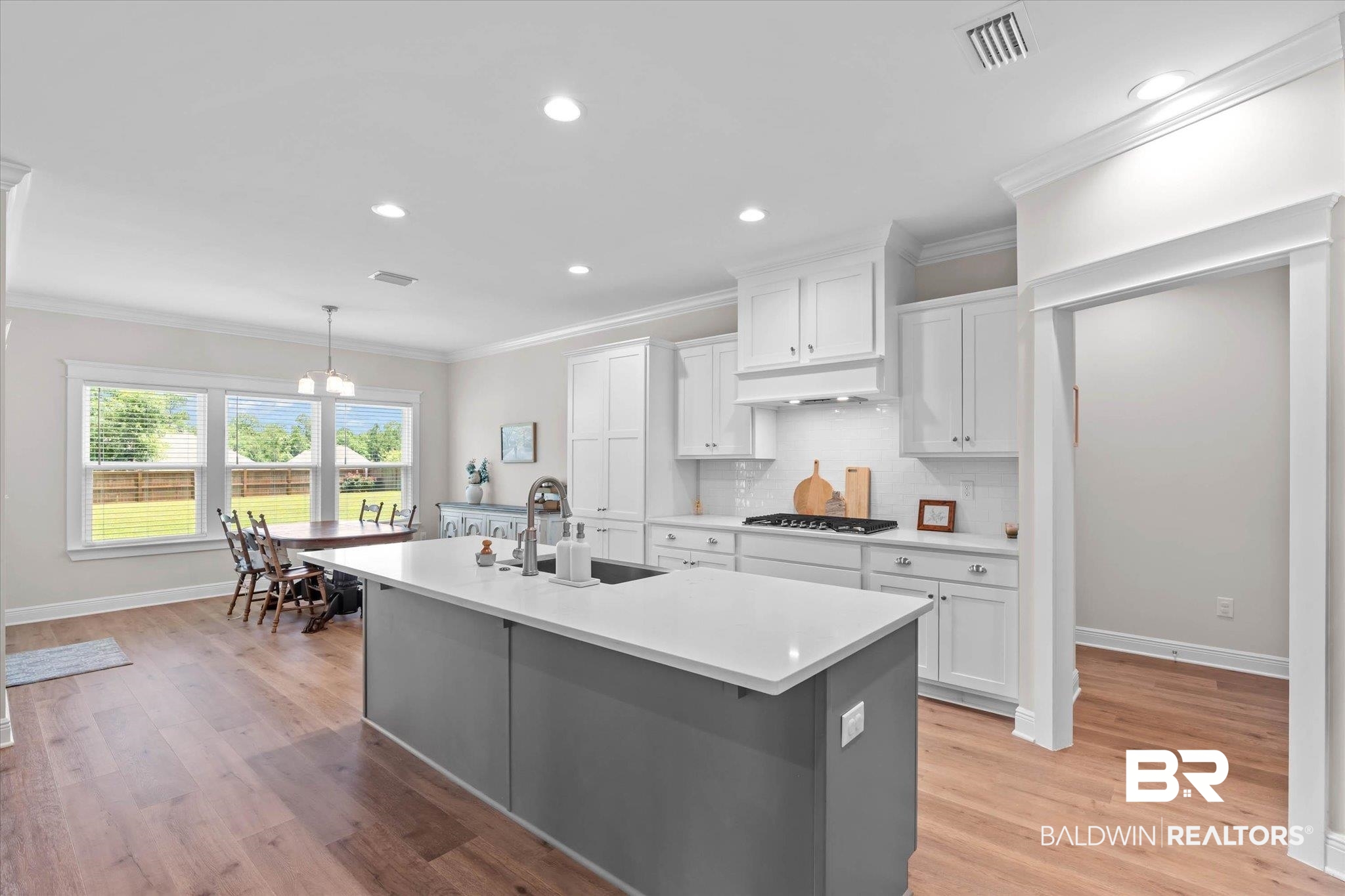 23523 Travis Stock Street Foley, AL 36535 - Photo 8 of 45 Modern kitchen featuring a large island with a light-toned countertop, white cabinetry, a gas range, and wood-finish flooring