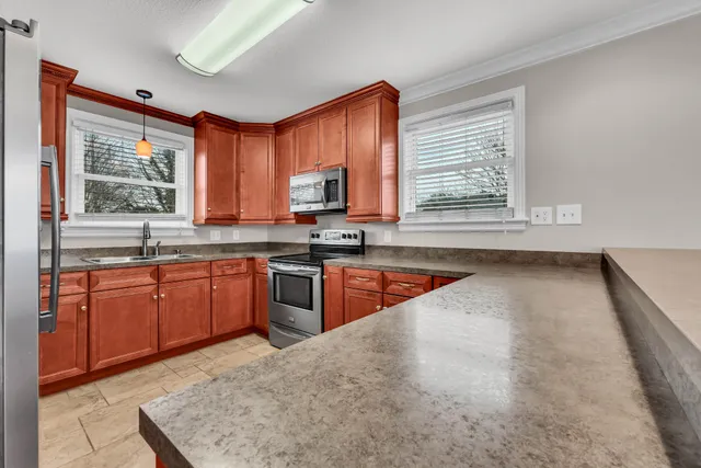 a large kitchen with stainless steel appliances granite countertop wooden cabinets a stove a sink and a large window