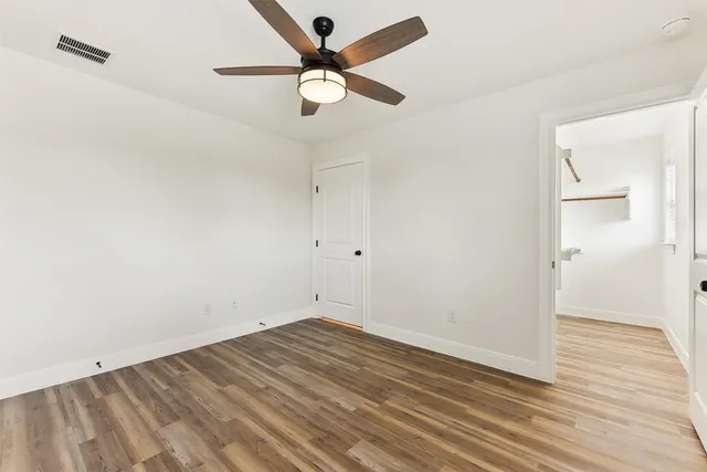 an empty room with wooden floor and a ceiling fan