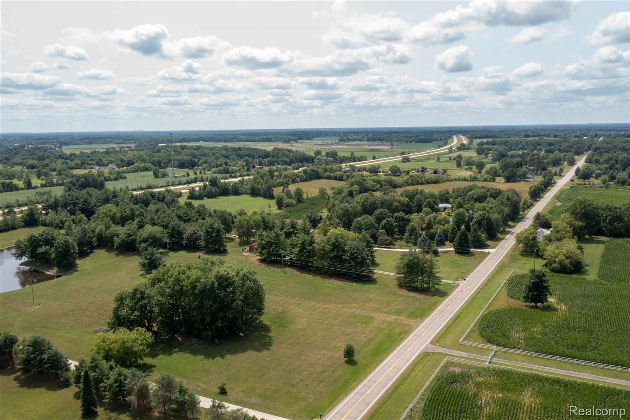 5761 Genesee Road Lapeer, MI 48446 - Photo 35 of 52 Expansive rural landscape featuring a pond, mature trees, open fields, and a paved roadway