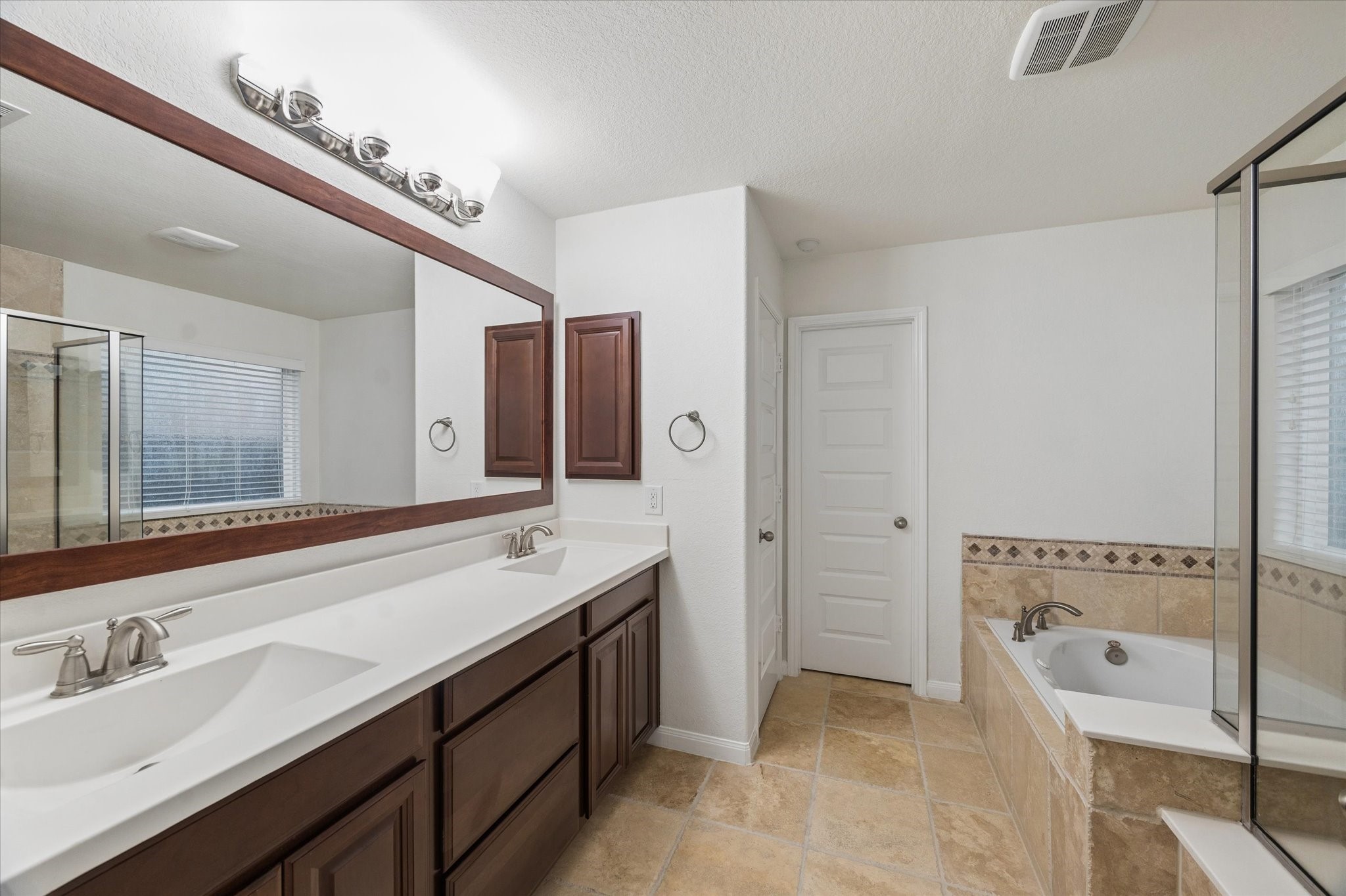 7015 Riata Hills Lane Spring, TX 77379 - Photo 16 of 33 The primary ensuite offers a spacious, spa-like retreat with a separate shower and soaking tub, complemented by warm wood finishes and soft, light-toned walls for a refined and serene atmosphere.
