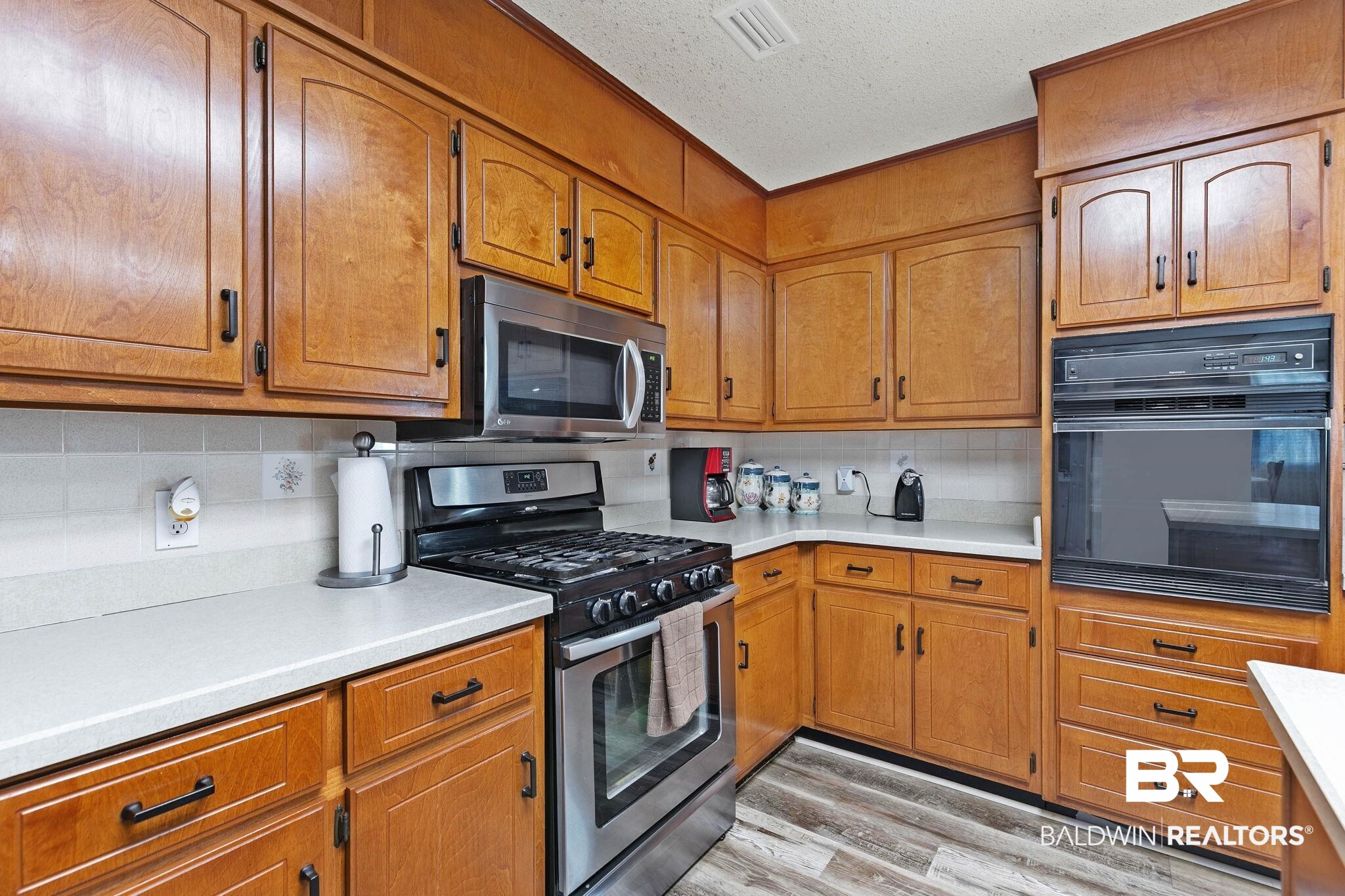 1510 South Juniper Street Foley, AL 36535 - Photo 15 of 36 Kitchen with appliances with stainless steel finishes, brown cabinetry, tasteful backsplash, light wood finished floors, and a textured ceiling