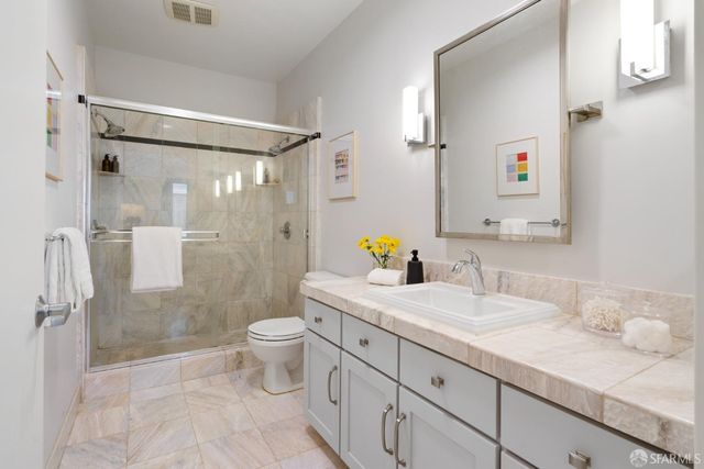 a bathroom with a granite countertop sink a toilet a mirror and shower