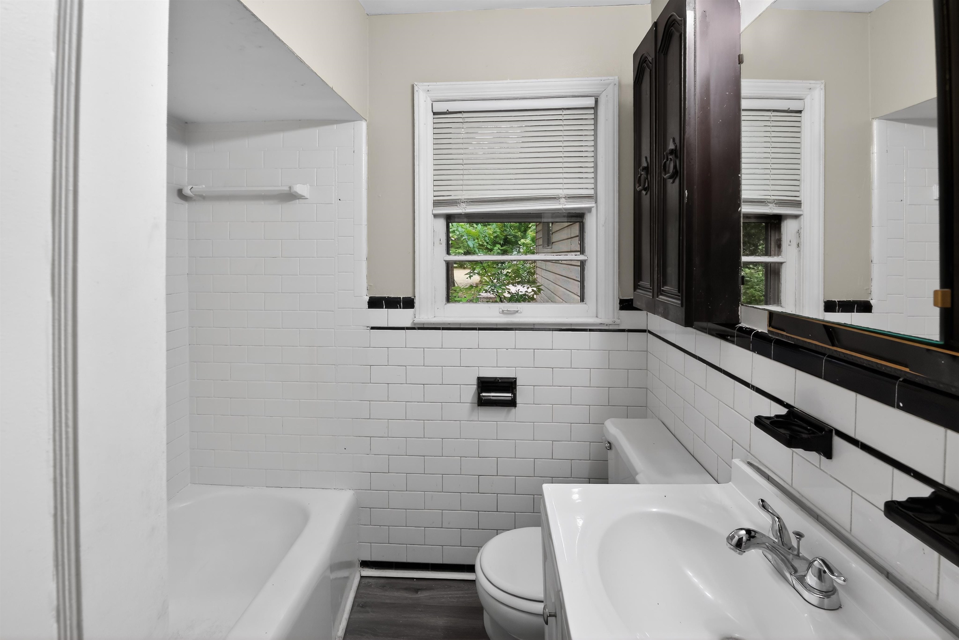 2840 Allen Road Memphis, TN 38128 - Photo 28 of 31 Bathroom featuring white subway tile walls with black trim, a bathtub with a tiled surround, and wood-finish flooring
