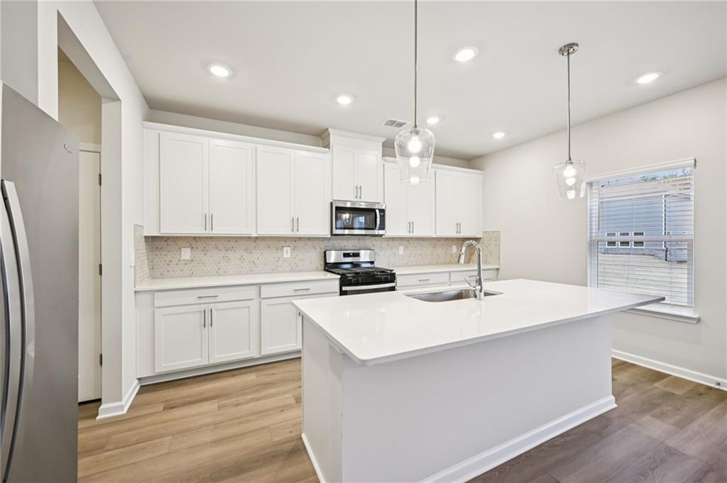 1408 High Fls Lane Grayson, GA 30017 - Photo 14 of 48 a kitchen with kitchen island a sink a stove a refrigerator and white cabinets with wooden floor