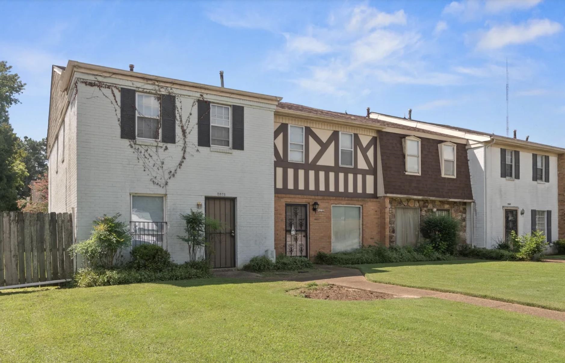 Townhome exterior featuring a white brick facade with black window shutters and a security storm door