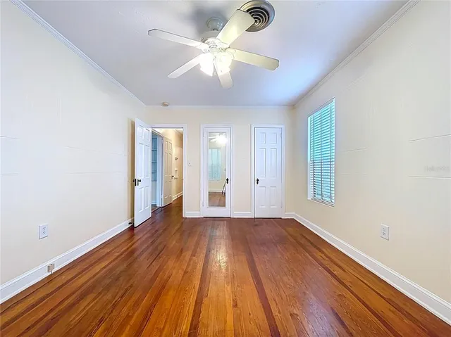 a view of an empty room with window a ceiling fan and wooden floor