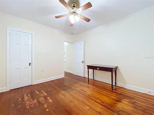 a view of an empty room with chandelier fan and wooden floor