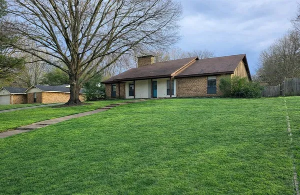 a view of a house next to a big yard and large trees