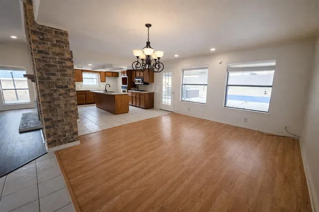an empty room with wooden floor chandelier and windows