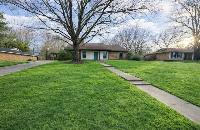 a brick house with garden and large trees