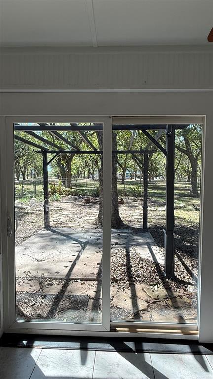 8513 Ravenswood Road Granbury, TX 76049 - Photo 12 of 21 Sliding glass patio door with a concrete patio and a metal pergola, surrounded by mature trees. This is set up to be a dream backyard.