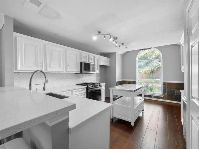 a kitchen with stainless steel appliances granite countertop a stove top oven a sink dishwasher and white cabinets with wooden floor