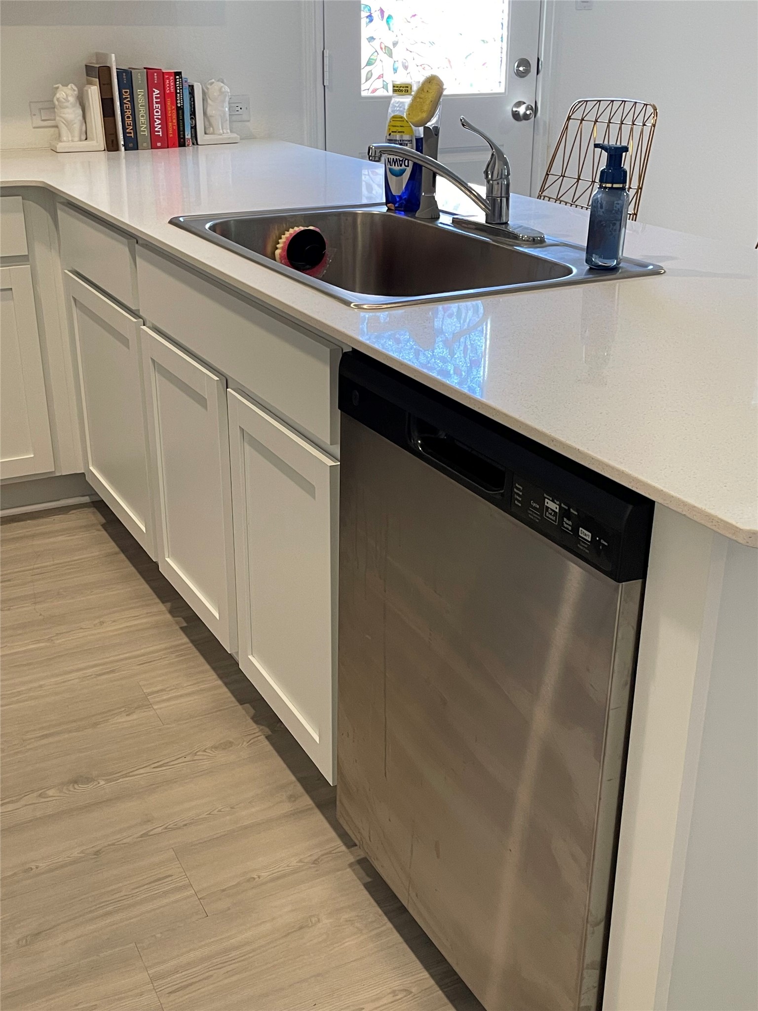 212 Marty Allen Loop Jarrell, TX 76537 - Photo 8 of 13 Kitchen island featuring a stainless steel sink with a single-handle faucet, integrated stainless steel dishwasher, white shaker-style cabinetry, light-toned countertops, and wood-finish flooring