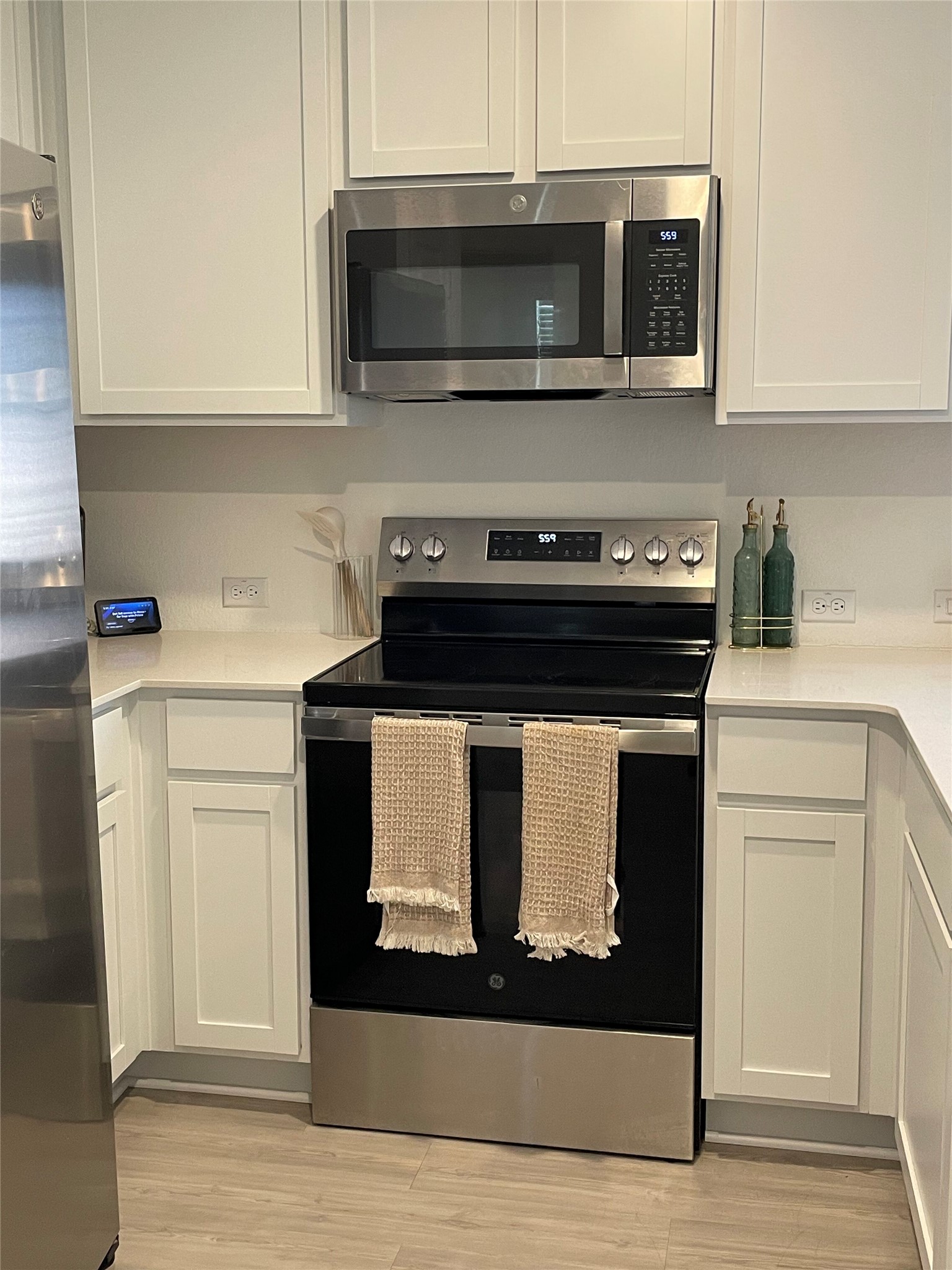 212 Marty Allen Loop Jarrell, TX 76537 - Photo 9 of 13 Kitchen featuring a stainless steel range with a black cooktop, an over-the-range microwave, white shaker-style cabinetry, light-toned countertops, and wood-finish flooring