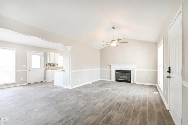 an empty room with wooden floor fireplace and windows