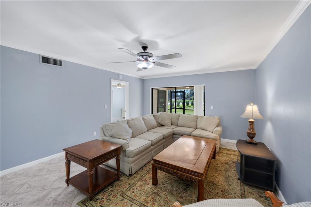 5857 Rattlesnake Hammock Road, Unit 101 Naples, FL 34113 - Photo 4 of 19 Spacious living area featuring light blue walls, a ceiling fan with integrated lighting, and crown molding