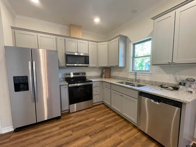 a kitchen with granite countertop a refrigerator stove a sink and dishwasher with wooden floor