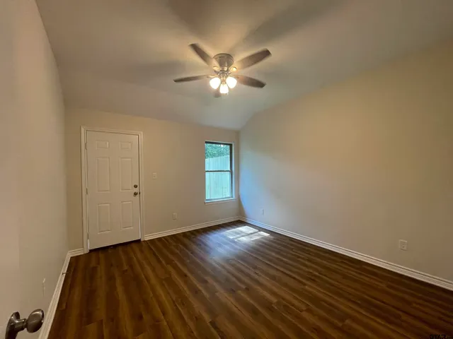 a view of an empty room with wooden floor and a ceiling fan