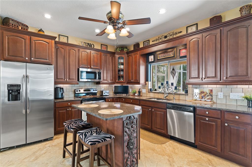 4202 Rotherham Court Palm Harbor, FL 34685 - Photo 14 of 61 a kitchen with stainless steel appliances granite countertop a stove top oven a sink dishwasher a dining table and chairs with wooden cabinets